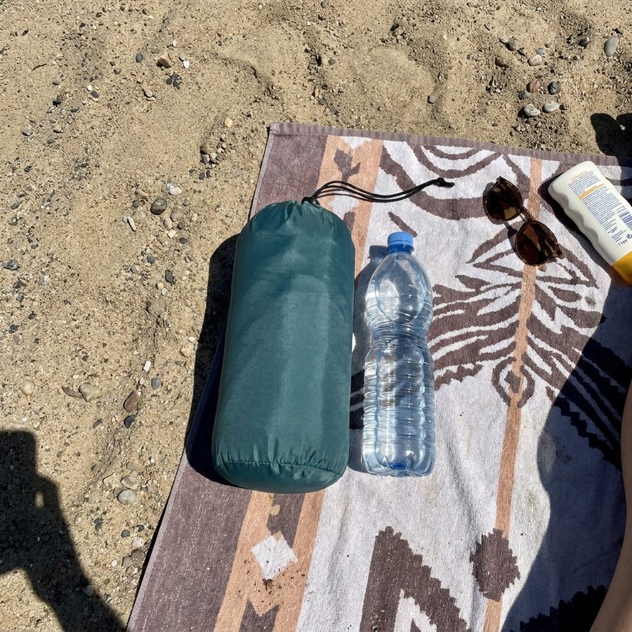 Gepackte Isomatte neben einer 1-Liter-Wasserflasche im Sand