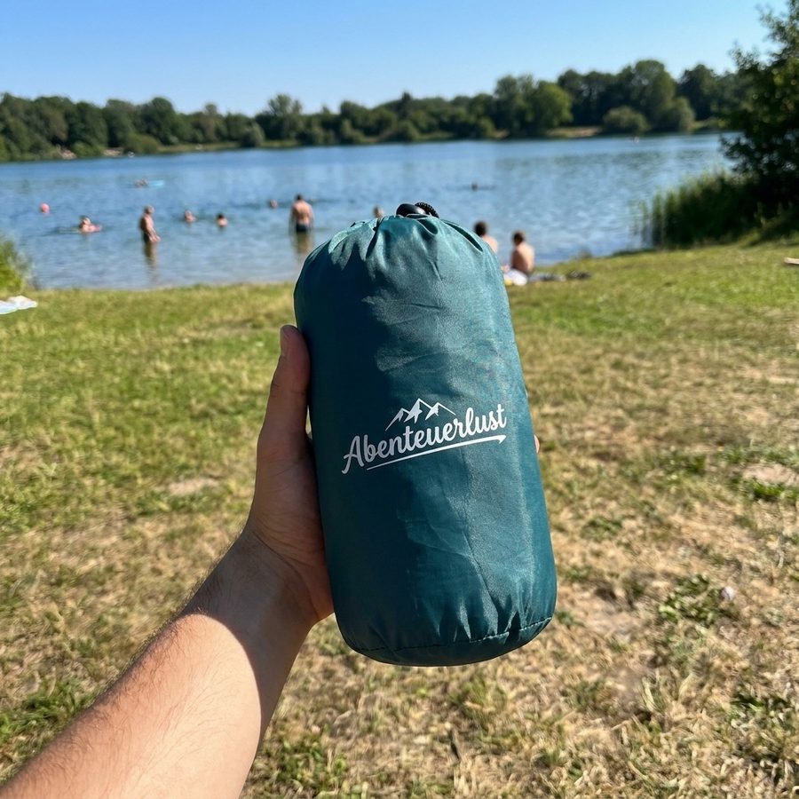 Packsack der Matte in einer Hand, im Hintergrund der See